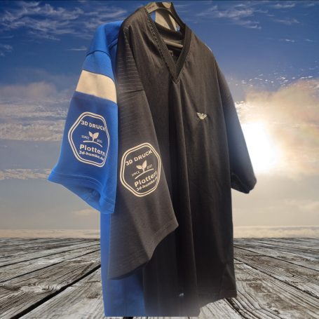Zwei T-Shirts, eins blau mit Aufdruck, eins schwarz, vor einem sonnigen Himmel.
