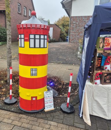 Ein rot-gelbes Leuchtturmmodell steht auf dem Gehweg neben einem Stand.