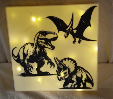 Drei beleuchtete Dinos: Tyrannosaurus, Flugsaurier und Triceratops auf hellem Hintergrund.