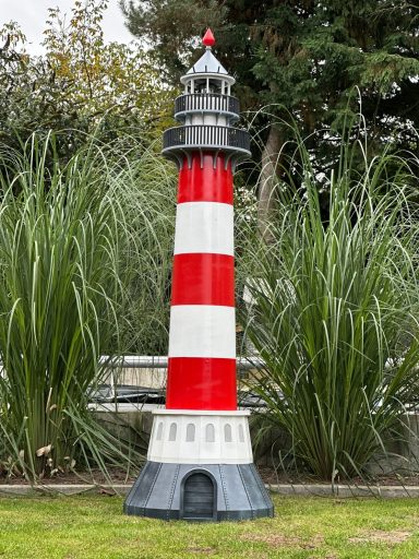 Ein rot-weißer Leuchtturm steht zwischen hohen Gräsern.