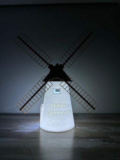 Windmühle mit beleuchtetem Sockel, in einem dunklen Raum präsentiert.