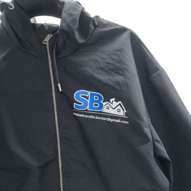 Schwarze Jacke mit blauem „SB“-Logo und Website-Adresse auf der Brust.
