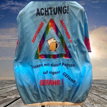 Bunte Jacke mit Warnhinweisen und Bier-Symbol, vor einem sonnigen Hintergrund.