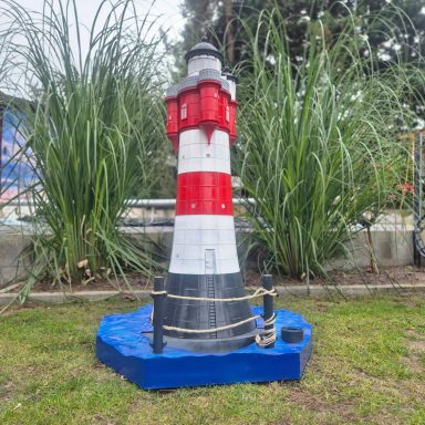 Bunter Leuchtturm mit rot-weißer Streifenmuster, umgeben von hohem Gras.