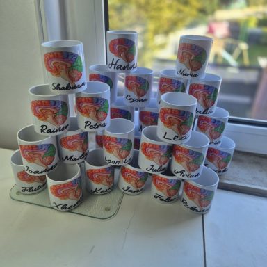 Eine Ansammlung von Tassen mit bunten Aufdrucken, auf einem Glasständer gestapelt.