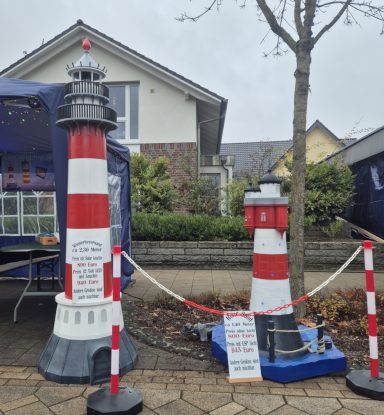 Zwei bunte Leuchttürme stehen auf einem Gehweg, neben einem Wohnhaus.