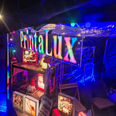 Bunte Lichter und der Schriftzug "PintaLux" über einem Verkaufsstand.